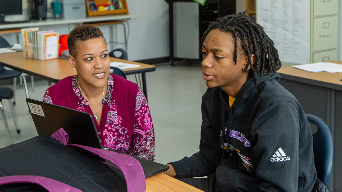 High school educator working with a student near his laptop.