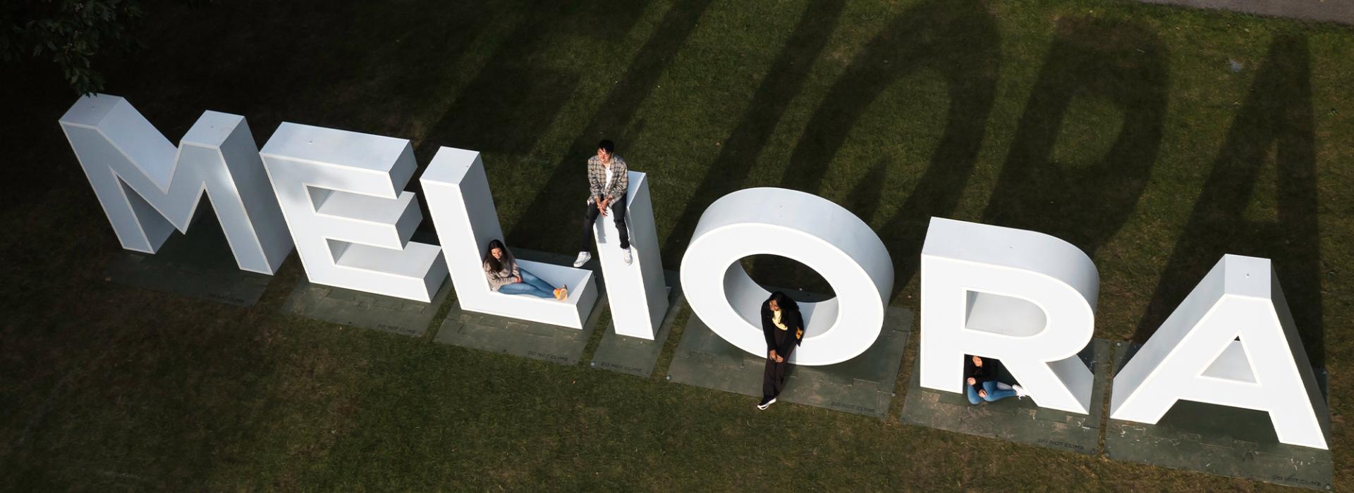 Ariel view of "Meliora" sign with students sitting on it
