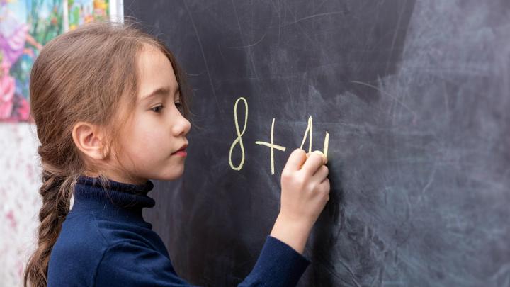 Elementary age girl writing math equation on chalk board