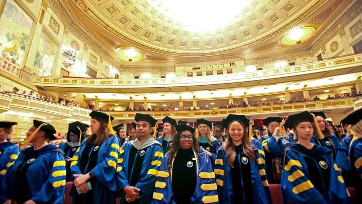 2025 Warner graduates standing in Kodak Hall at Eastman Theater.
