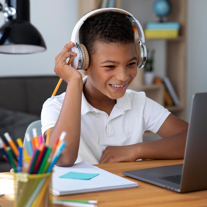 Child is on computer wearing headphones and smiling