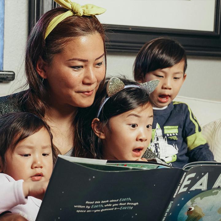 Female adult reading a book about Earth to three young children.