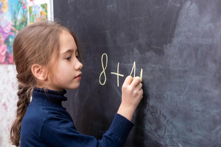 Elementary age girl writing math equation on chalk board
